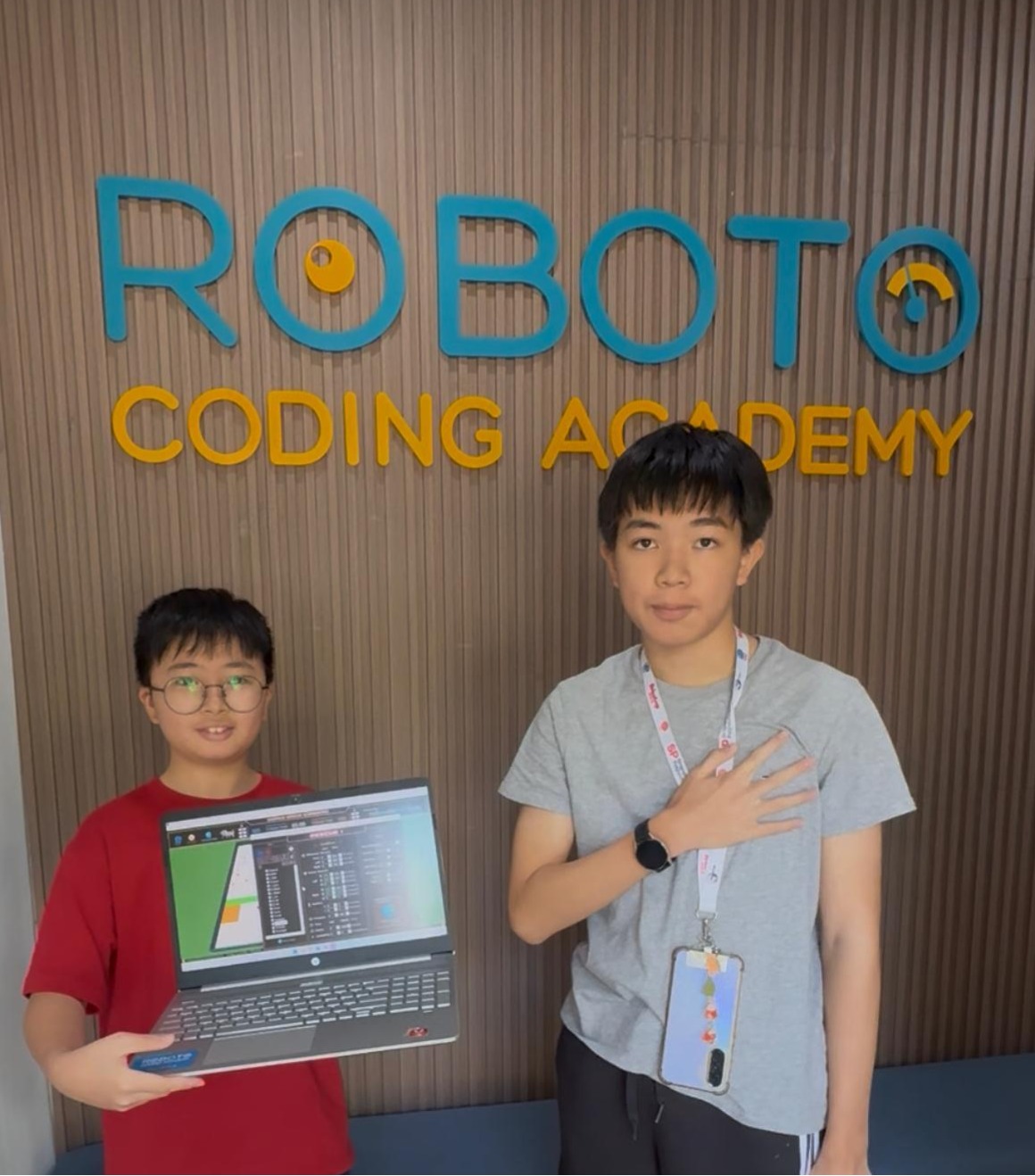 Students showing laptop project at Roboto Coding Academy sign