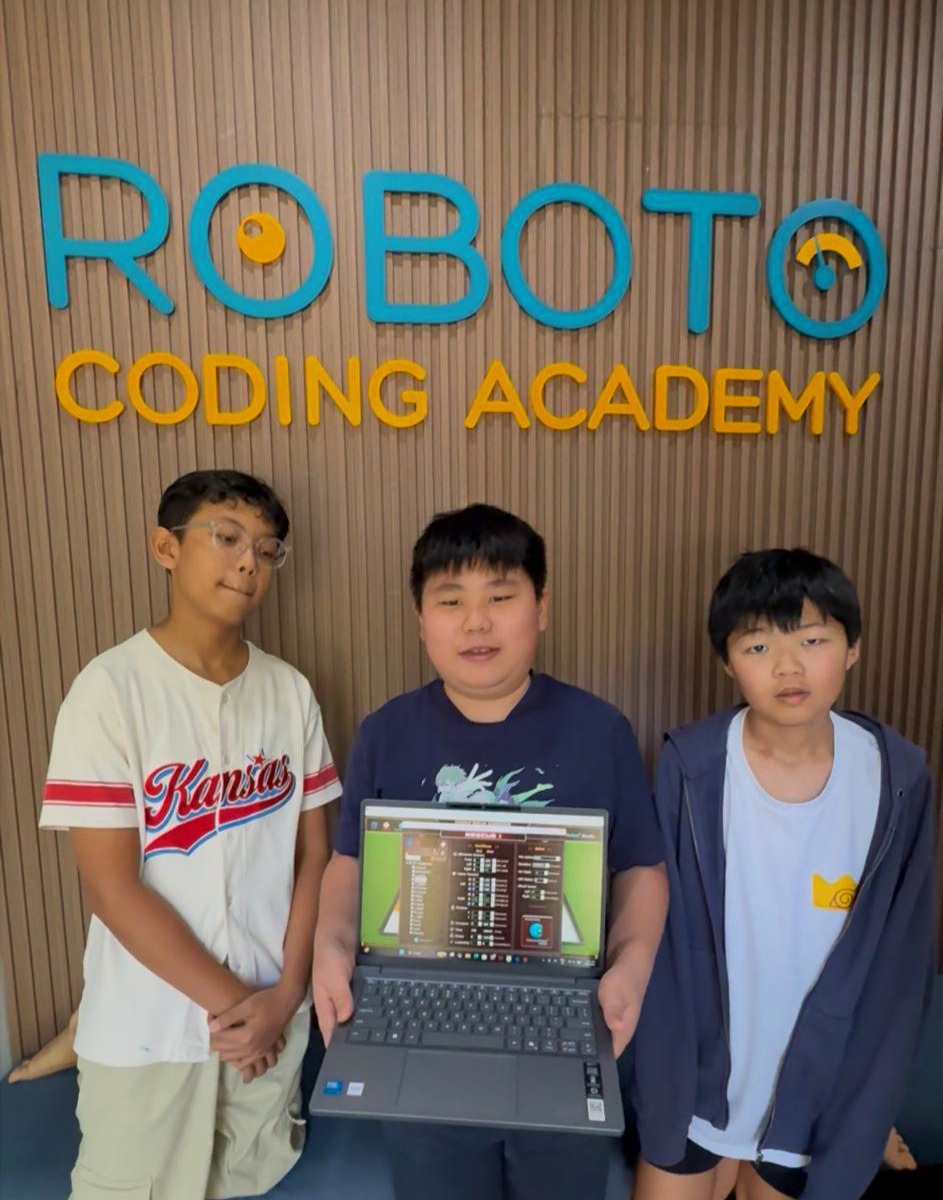 Three students with laptop at Roboto Coding Academy sign